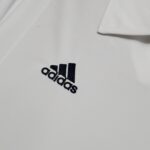 30ba54e8_c41f6699-8f90-445c-8458-9e2df11e83f9 | UAE SPORT STORE Close-up of white fabric with the Adidas logo partially visible in black letters, cropped at the bottom.