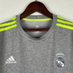 Gray sports shirt on a hanger featuring a Real Madrid crest and neon-yellow shoulder stripes with an Adidas logo nearby.