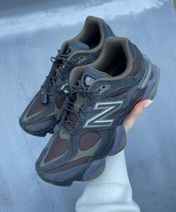 31027769-4664-4858-a6e4-8e360767e56f | UAE SPORT STORE Dark gray New Balance 901 trail sneakers with brown overlays, held in a hand against a gray background, showing the 'N' logo and rugged sole