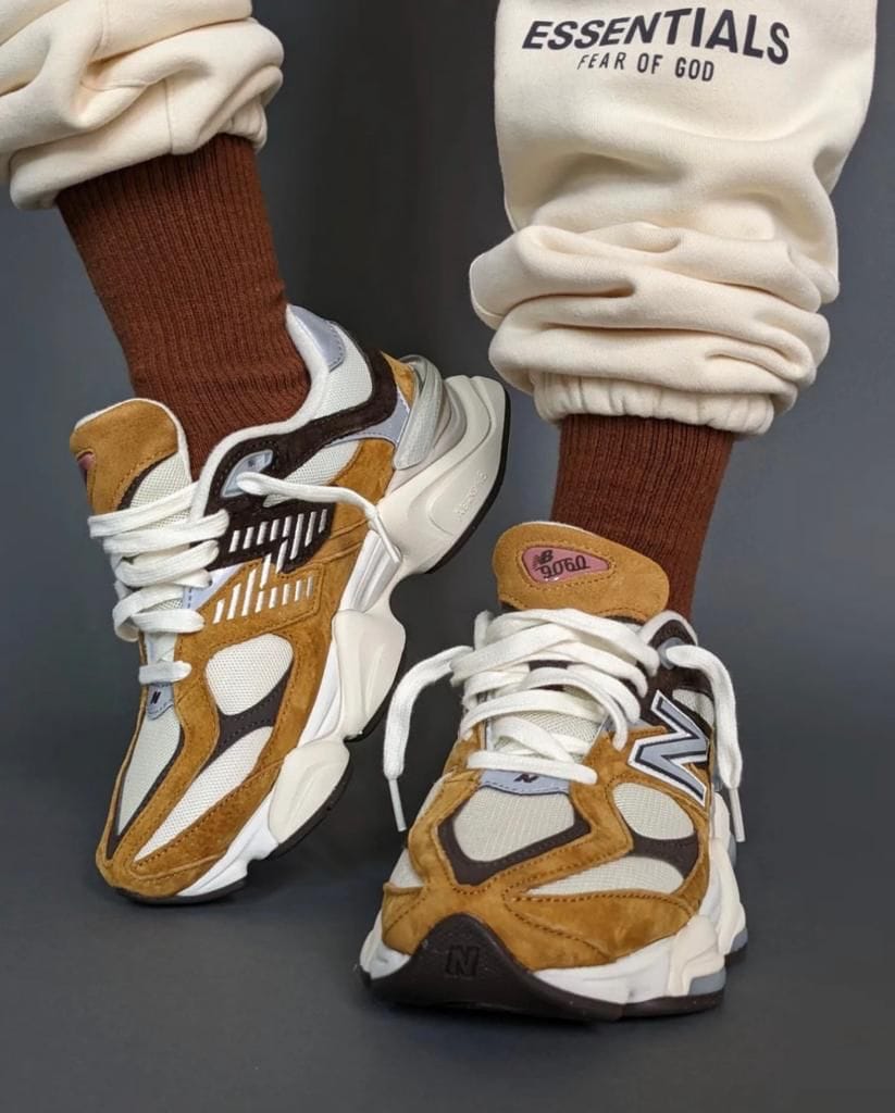 3103d358-4e25-4d5d-89ae-30a269d0b3fb | UAE SPORT STORE Pair of tan, white, and gray sneakers with suede accents, worn with brown crew socks and cream joggers that say 'ESSENTIALS FEAR OF GOD'.