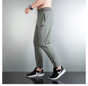 Side view of a person wearing gray Under Armour joggers with a zippered ankle and a black Nike-style athletic shoe
