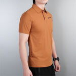 Man wearing an orange polo shirt with a small black Nike swoosh, shown from the side against a gray wall.