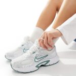 Person tying white athletic sneakers with teal Nike swoosh, wearing white socks and rolled-up pants.