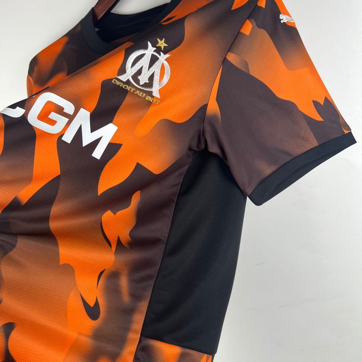 Close-up of an orange and black camouflage-patterned jersey with a white embroidered club crest and a gold star above it.