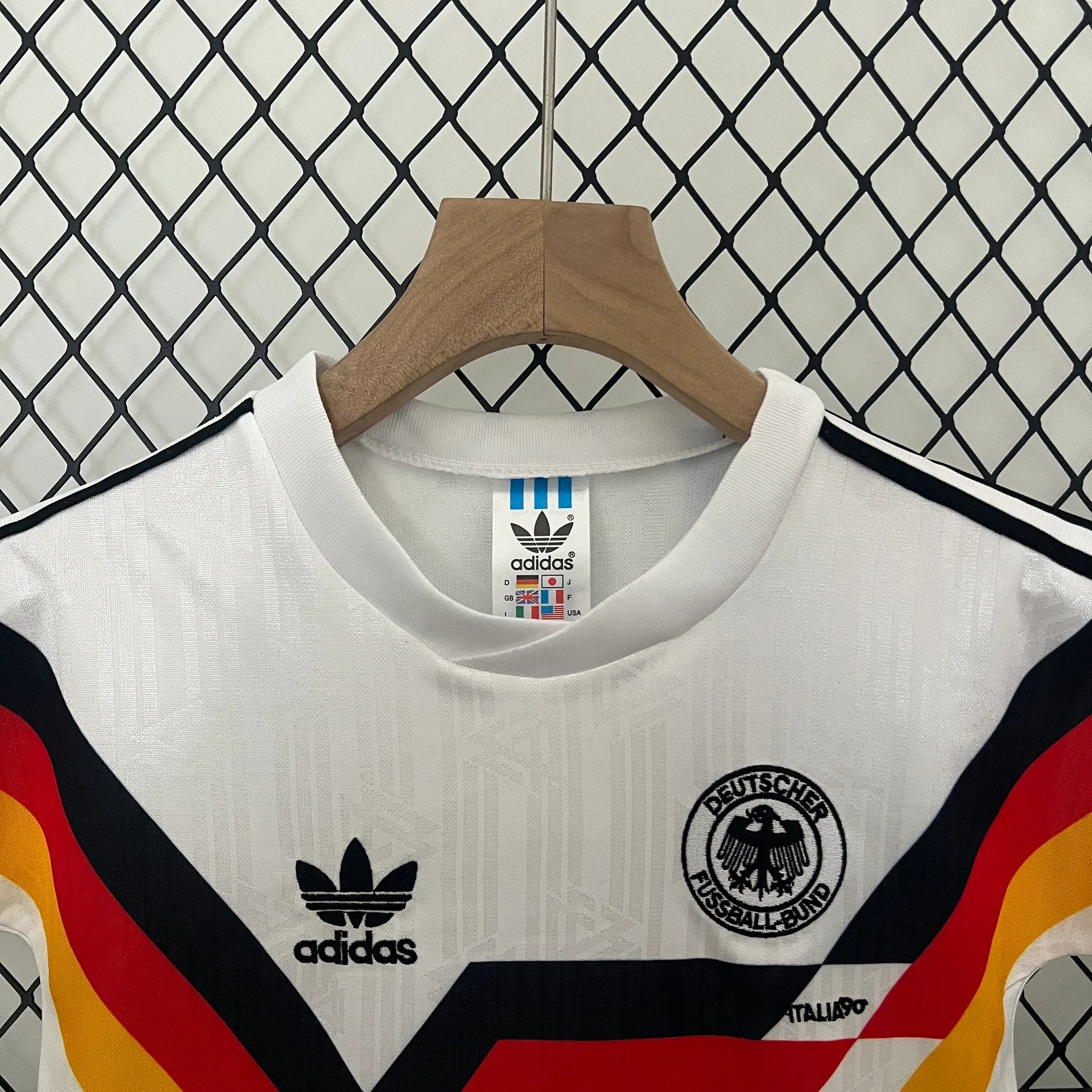 31d66ae9 | UAE SPORT STORE White Germany national football jersey on a wooden hanger, Adidas logo and DFB crest visible, with bold black, red, and yellow diagonal stripes in the foreground.