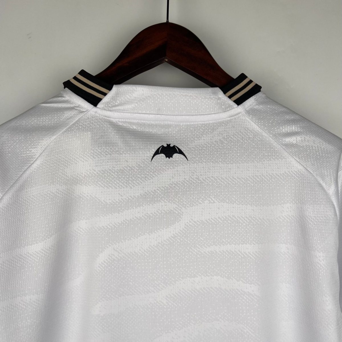 White polo shirt on a wooden hanger with a Batman logo on the chest.