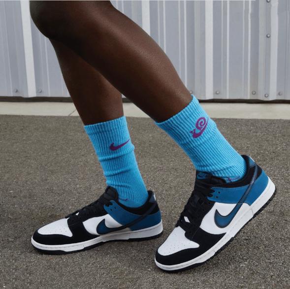 Close-up of blue crew socks with pink logos paired with white, black, and blue Nike sneakers on pavement.