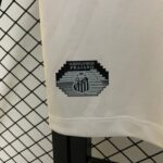 Close-up of white textured fabric with a black shield logo reading 'GLORIOSO ALVINEGRO PRAIANO' and a dark chair leg, with a chain-link fence in the background.