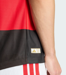 3333_3486bea2-2762-4577-b29f-b82114a9d608 | UAE SPORT STORE Close-up of a red and black Adidas jersey hem with a gold Authentic Licensed Product tag.