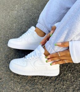 Person wearing white Nike sneakers with gray sweatpants, adjusting cuffs with lime-green manicured nails visible.