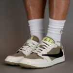 Beige and white Nike sneakers with a black swoosh, worn with high white socks against a gray backdrop.