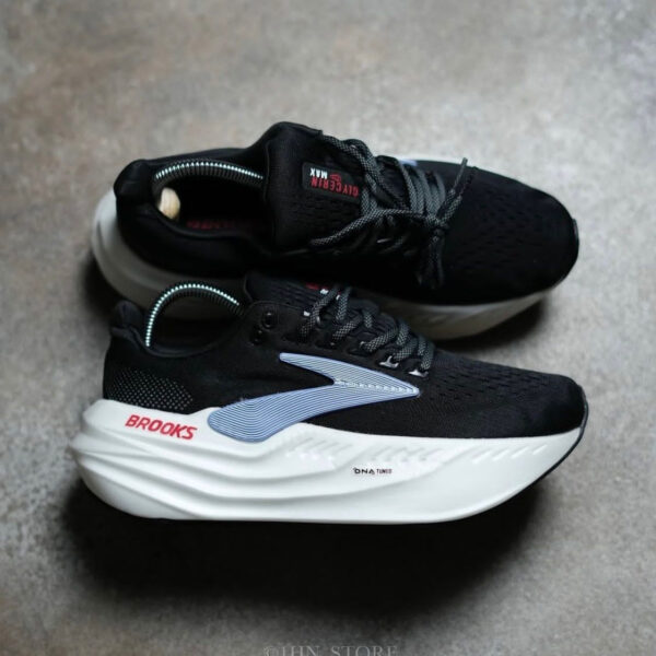 Pair of black Brooks running shoes with white chunky midsoles on a gray floor; red Brooks branding on the heel and light blue side accent.