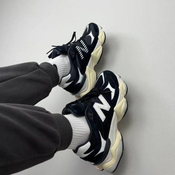 Casual black and white chunky sneakers with white socks resting against a light wall.