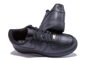 Black Nike Air sneakers, low-top, side Swoosh, photographed with one shoe resting on the other for a studio product shot.