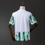 Back view of a white athletic jersey with green tropical leaf print on the sleeves and hem, shown on a mannequin's torso.
