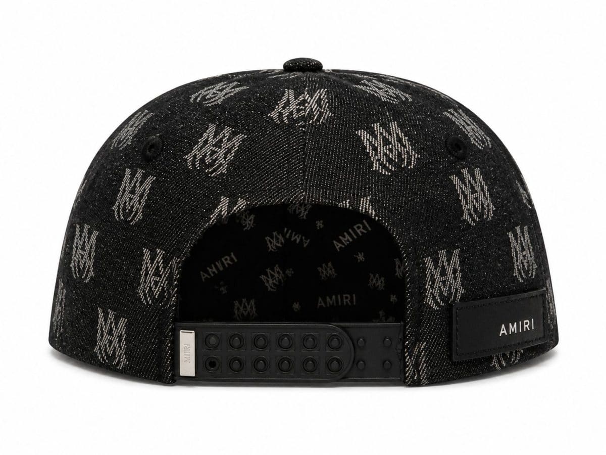 Back view of a black denim cap with an all-over AMIRI logo pattern, featuring an adjustable snap strap and a stitched AMIRI patch on the back.