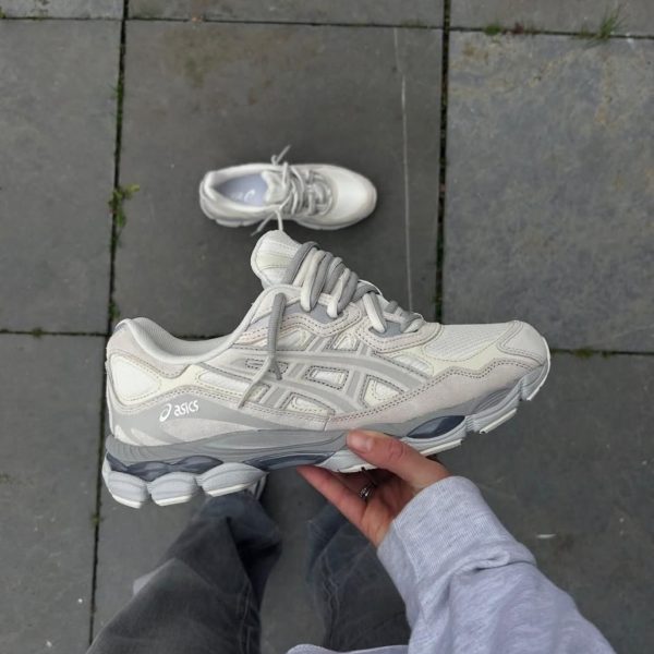 Top-down view of a person holding a light gray Asics running shoe, with a second matching shoe on a grey stone patio.