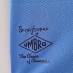 35386f2b_2c1eed1c-822c-43de-a153-11c996cb0a52 | UAE SPORT STORE Close-up of blue fabric showing a black Umbro sportswear stamp and the word 'Sportswear'