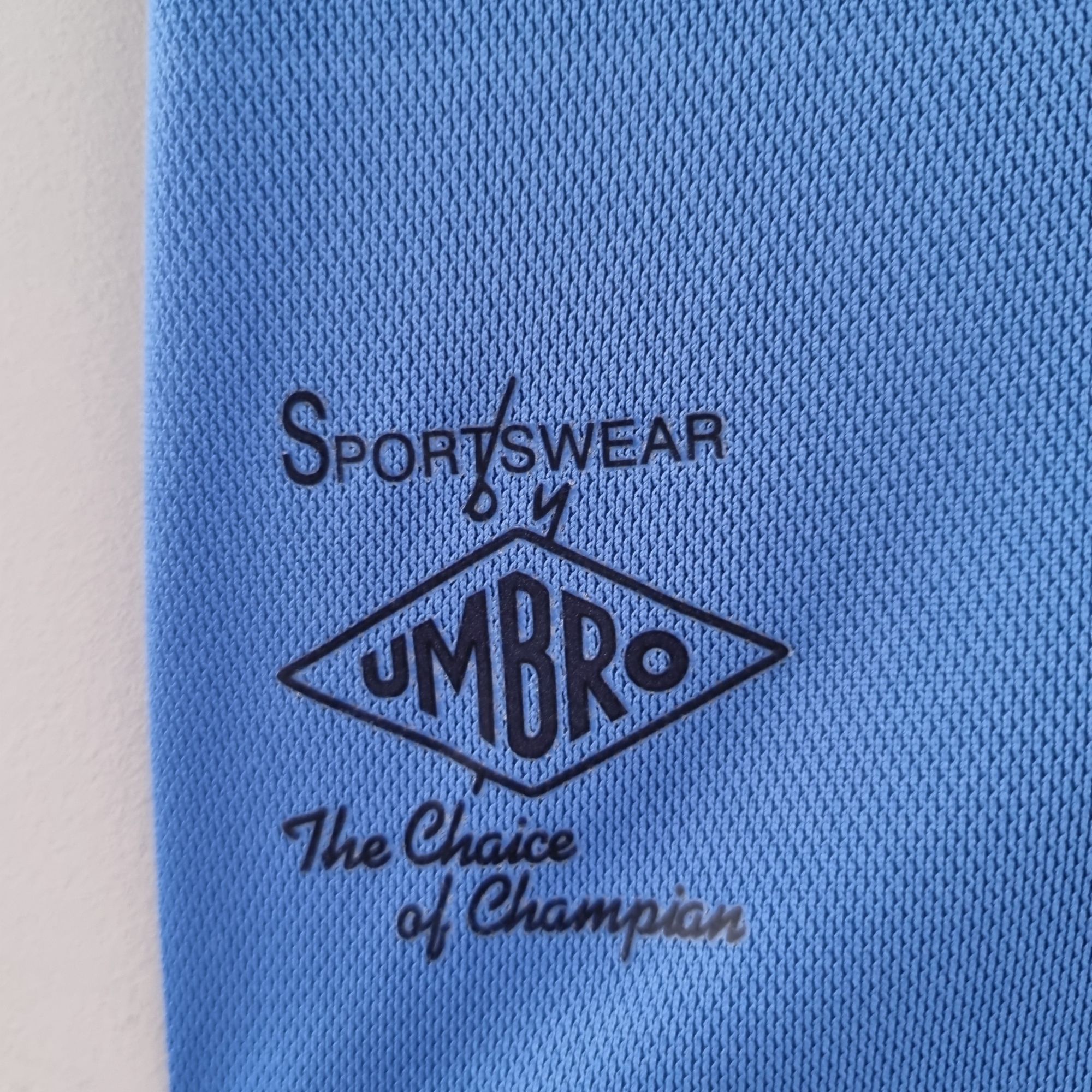 35386f2b_2c1eed1c-822c-43de-a153-11c996cb0a52 | UAE SPORT STORE Close-up of blue fabric showing a black Umbro sportswear stamp and the word 'Sportswear'