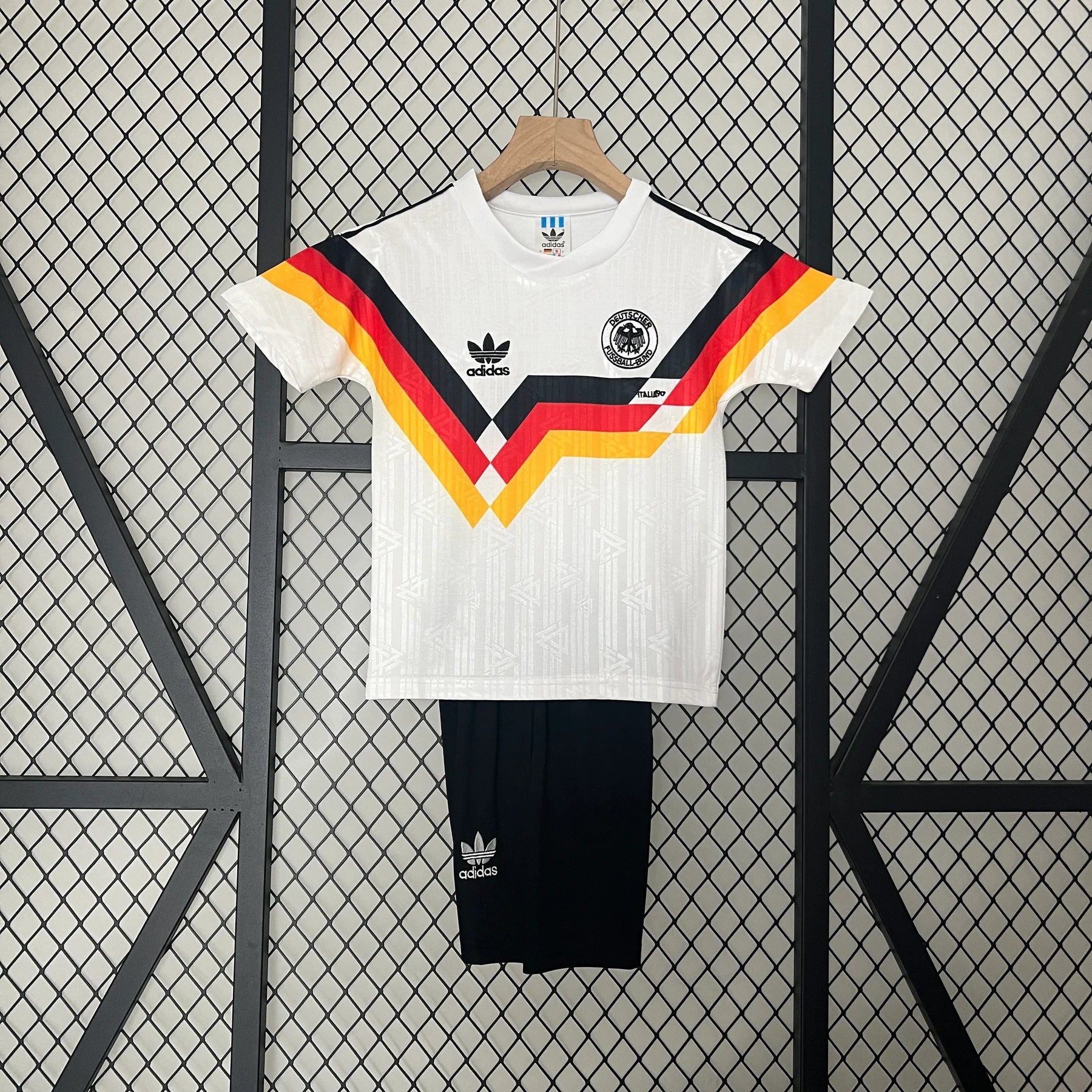 3541a1e8 | UAE SPORT STORE White Adidas Germany national team jersey on a wooden hanger, featuring black, red, and gold chevron stripes against a wire mesh backdrop.