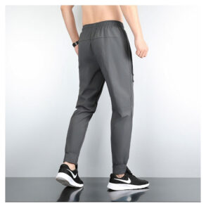 Back view of a man wearing gray jogger pants with an elastic waistband and side zip pocket, paired with black-and-white sneakers.