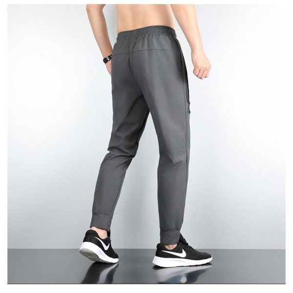 Back view of a man wearing gray jogger pants with an elastic waistband and side zip pocket, paired with black-and-white sneakers.