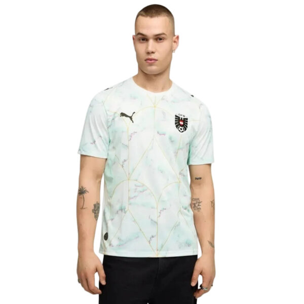 Male model wearing a light marble-patterned Puma jersey with a crest on the chest, standing against a white background; visible tattoos on arms.