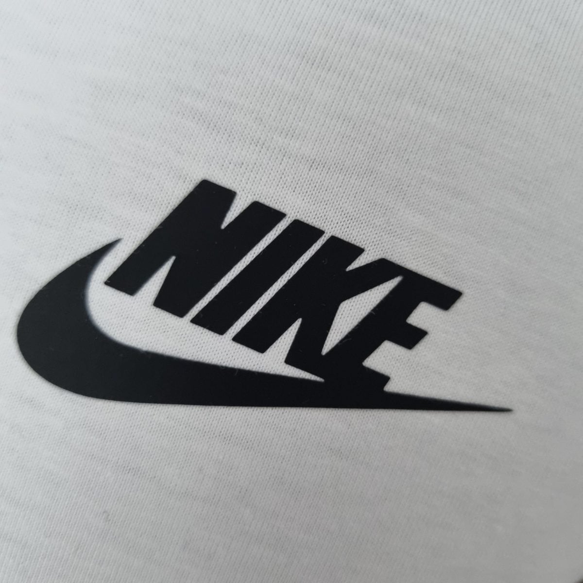 Close-up of white knitted fabric with a partial bold black graphic or lettering visible at the bottom edge.