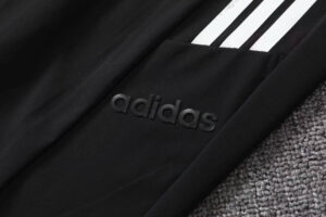Close-up of a black Adidas jacket pocket with embossed logo and three white stripes nearby.