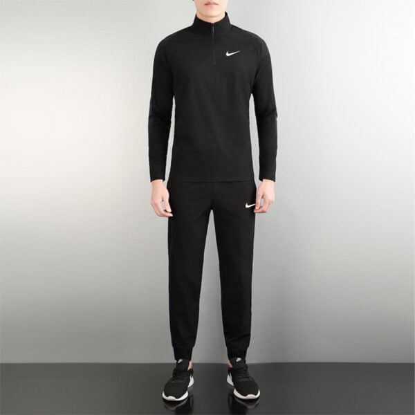 Person wearing a black Nike tracksuit with a white swoosh on the chest, standing against a gray background.