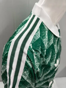 Close-up of a green patterned sports jersey with a white collar and three white stripes along the shoulder on a mannequin