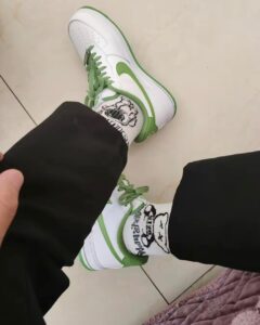 Top-down view of a person wearing white and green sneakers with green laces, black pants, and white socks with a panda graphic.