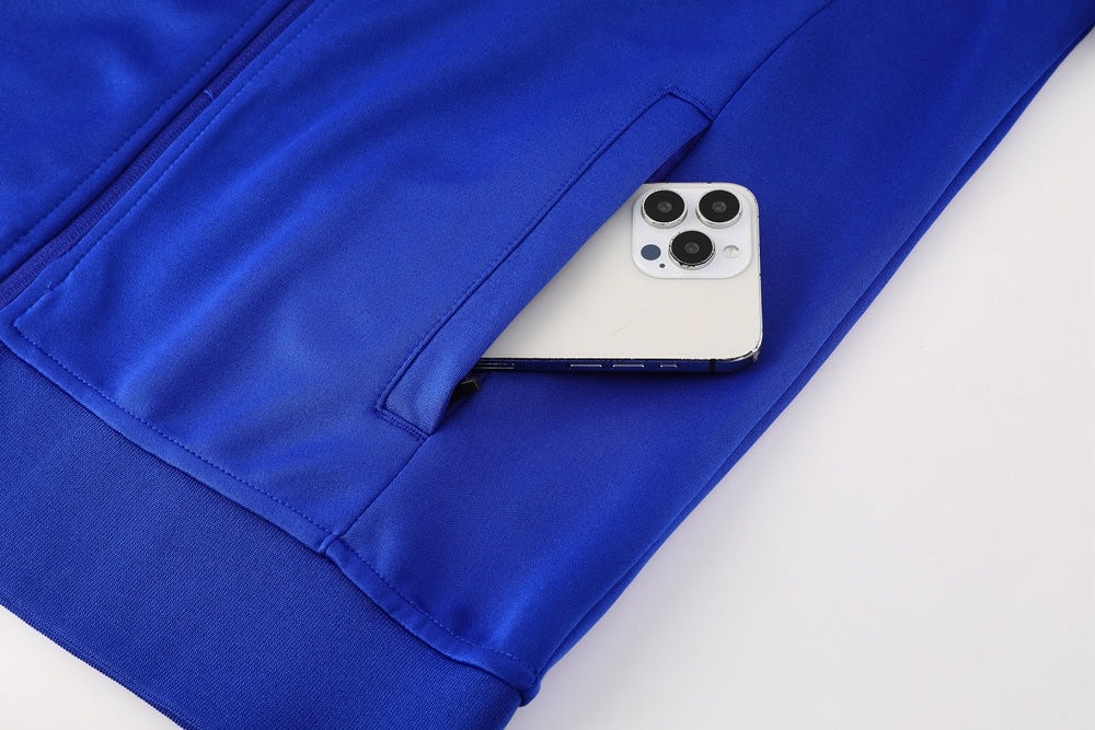 36ca654a | UAE SPORT STORE Blue zippered jacket with a white smartphone peeking out of a side pocket.