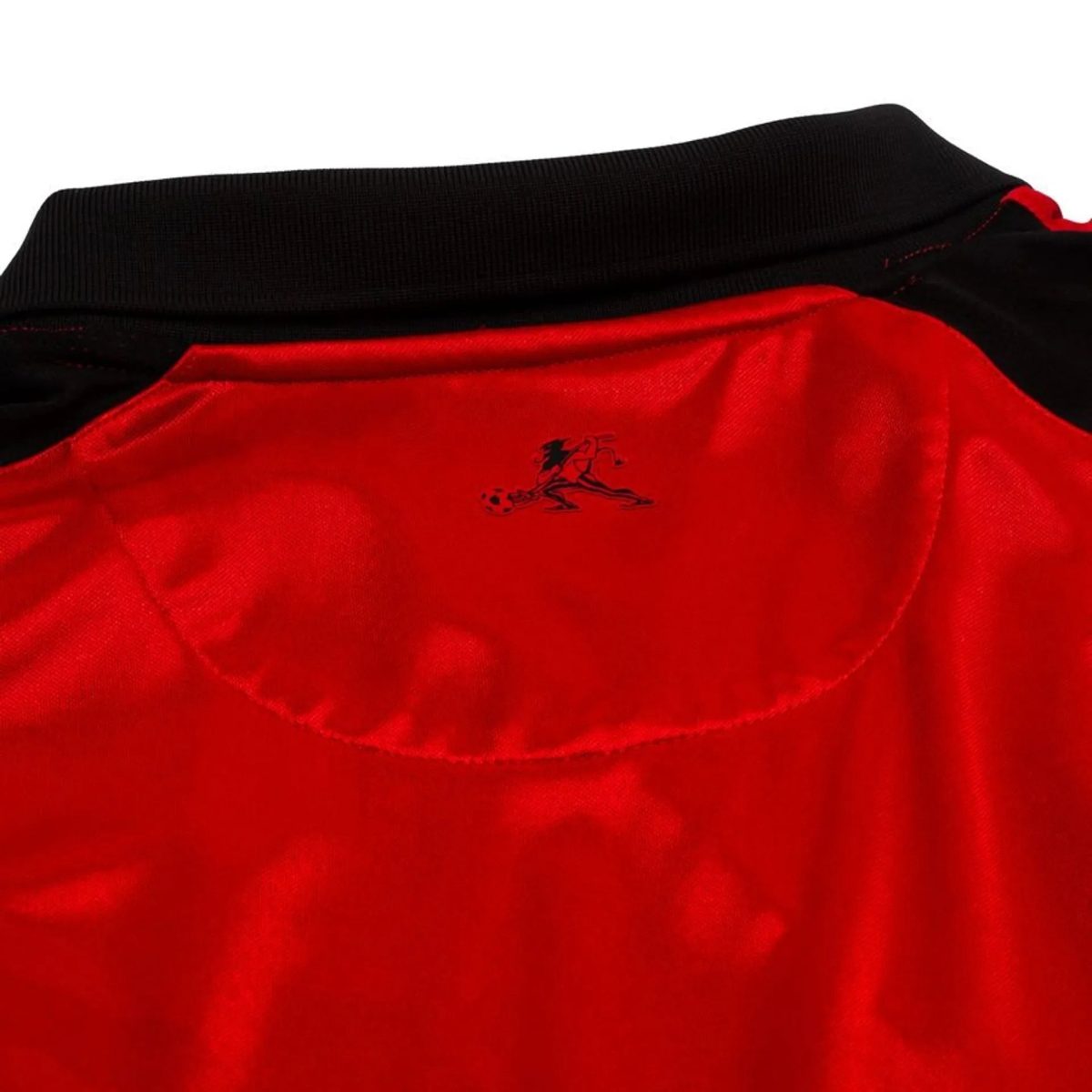 Close-up of a red athletic jersey with a black ribbed collar and a small black horse-and-rider emblem
