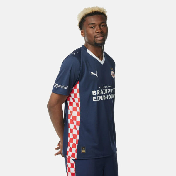 Male model wearing a navy blue football jersey with red-and-white checkered side panels and sponsor text across the chest, looking to the side.