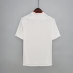 372b1360_82a00d41-f1fe-4e13-853f-995b31904c28 | UAE SPORT STORE White shirt on a wooden hanger against a gray wall, back view showing a red inner collar lining