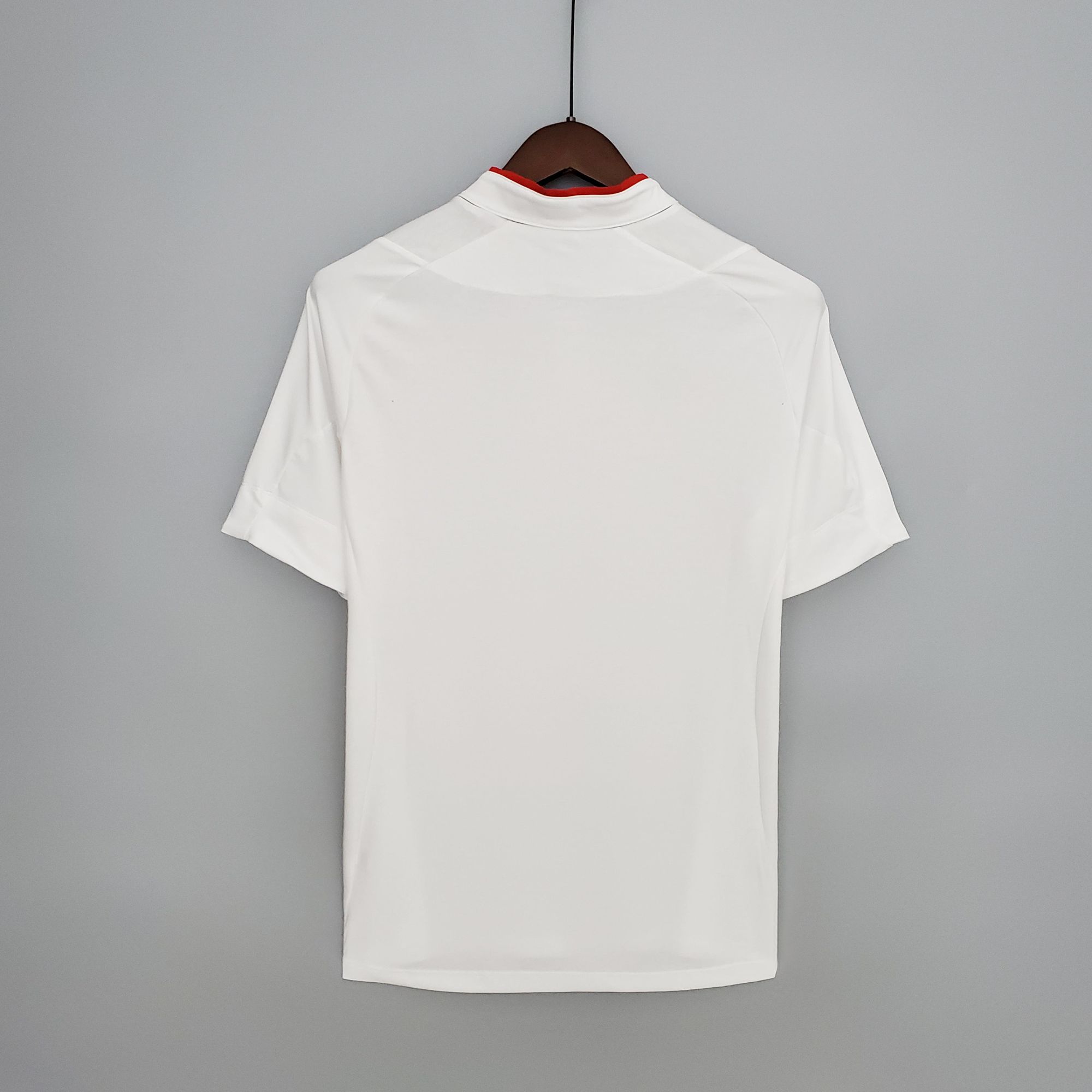 372b1360_82a00d41-f1fe-4e13-853f-995b31904c28 | UAE SPORT STORE White shirt on a wooden hanger against a gray wall, back view showing a red inner collar lining