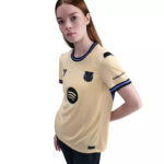 37612710_o_a2 | UAE SPORT STORE Young woman modeling a beige sports jersey with blue trim and sponsor logos on the chest and sleeve.