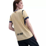 37612710_o_a3 | UAE SPORT STORE Back view of a woman wearing a beige UNHCR t-shirt with a small flag at the neck and blue trim, standing in profile.