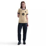 37612710_o_a4 | UAE SPORT STORE Female model wearing a beige athletic T-shirt with navy trim and patches, paired with black jogger pants and black sneakers, facing forward.