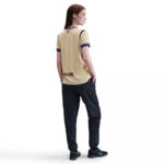 37612710_o_a5 | UAE SPORT STORE Rear view of a person wearing a beige UNHCR-branded T-shirt and dark pants, hands in pockets.