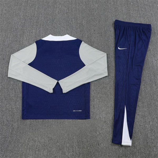 Two-piece athletic tracksuit: navy blue top with light gray sleeves and matching navy pants with a white Nike swoosh logo, laid flat on a gray surface.