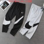 Two Nike joggers laid out side by side: black pants with a white swoosh and diagonal white panel, and light gray pants with a large black swoosh on the leg.