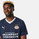 Man wearing a dark blue PSV Eindhoven football jersey with white V-neck, crest and two gold stars visible on the chest.