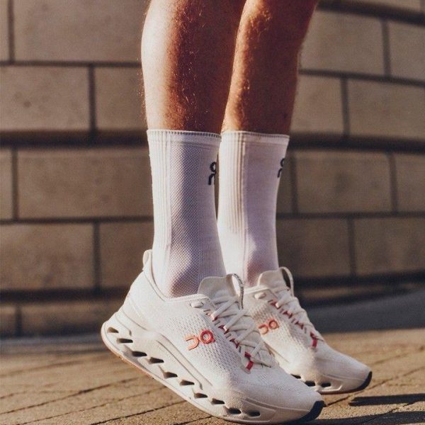 Pair of white athletic shoes with a hollow-cut sole and white crew socks on a person standing on a brick sidewalk.