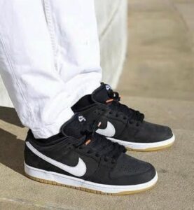 Black Nike sneakers with white swoosh on light-colored pavement, white pants visible above the shoes.