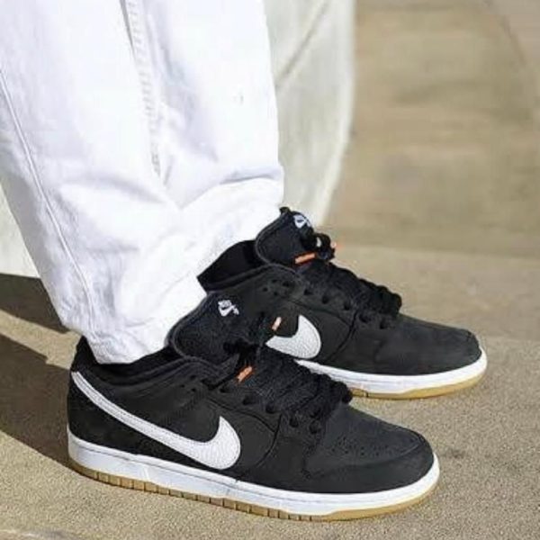 Black Nike sneakers with white swoosh on light-colored pavement, white pants visible above the shoes.
