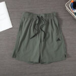 Olive green athletic shorts with black drawstring and Adidas logo on the left leg, laid flat on a wooden floor.