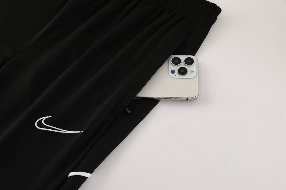 3948b0e8 | UAE SPORT STORE Close-up of black Nike athletic pants with a white swoosh logo, a silver iPhone tucked into the side pocket.