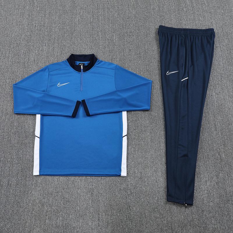 39852500-6f22-4df6-b99a-8a6edaab5ded | UAE SPORT STORE Blue Nike athletic jacket with half-zip and white side panels, paired with navy Nike track pants laid flat.